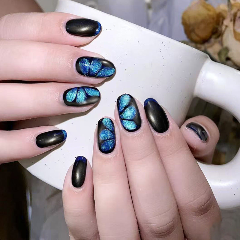 Hand with black and blue butterfly nail art holding a white mug.