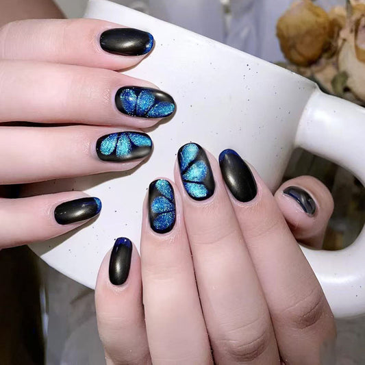 Hand with black and blue butterfly nail art holding a white mug.