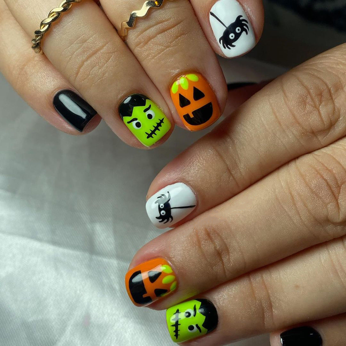 A set of press-on nails featuring a black, white, and orange color scheme with cartoonish monster designs, displayed on a person's hands.