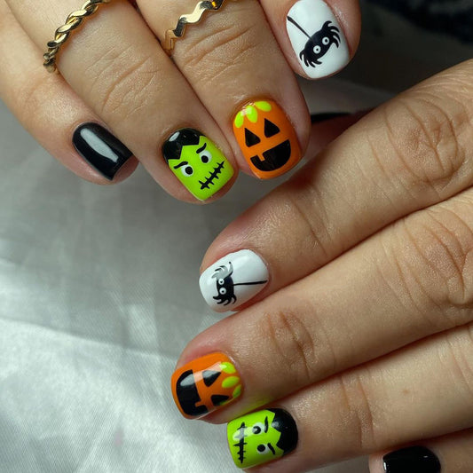 A set of press-on nails featuring a black, white, and orange color scheme with cartoonish monster designs, displayed on a person's hands.