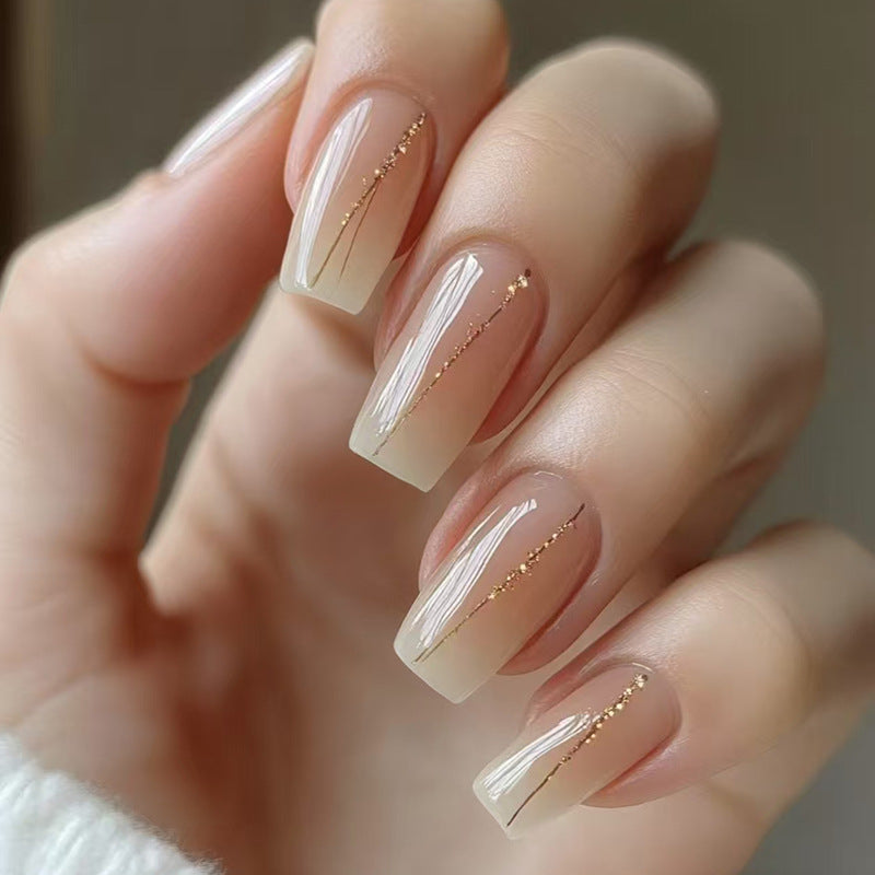 Close-up of a hand with beige nail polish and gold accents on a blurred background