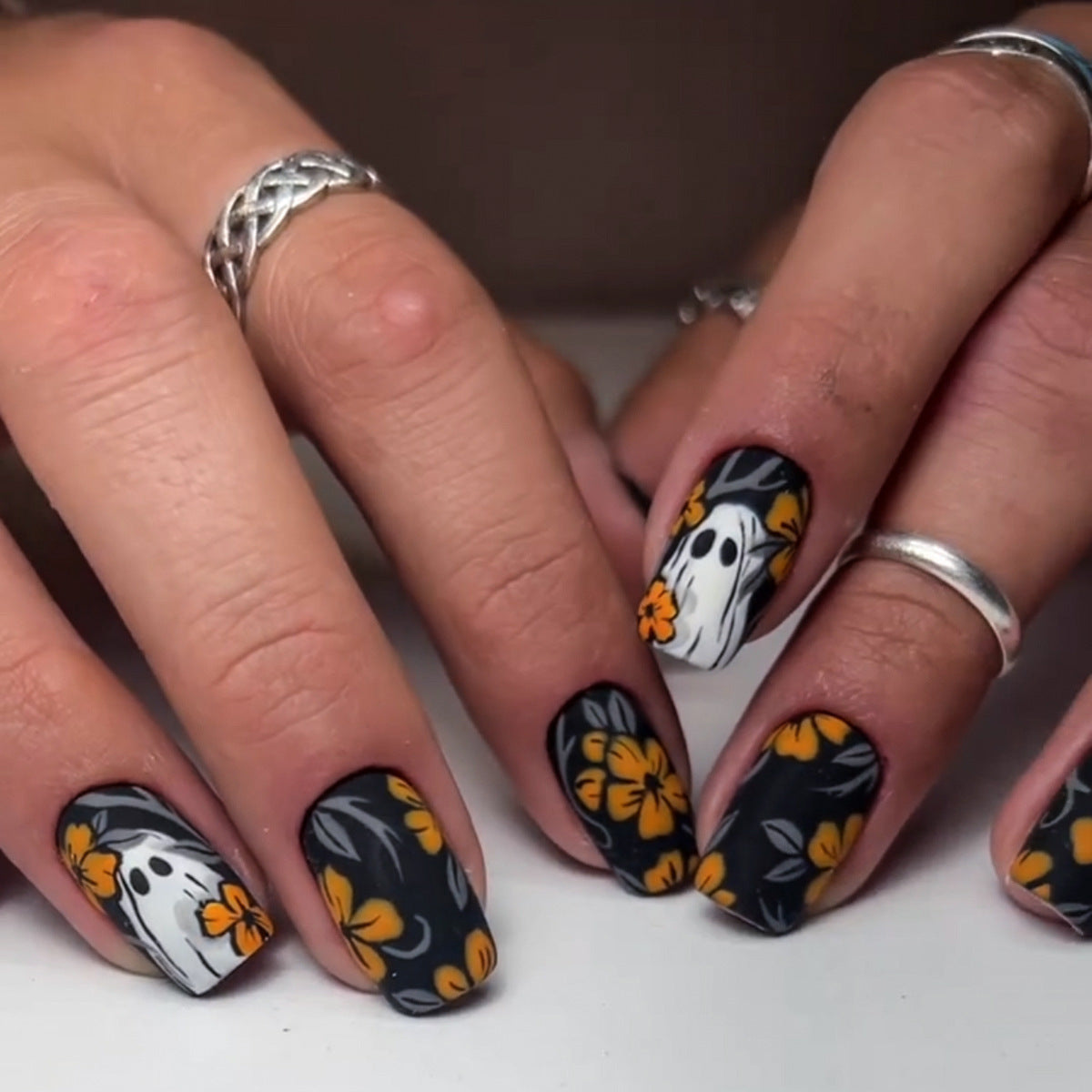 A set of press-on nails featuring a combination of black, orange, and yellow flowers with ghost designs.