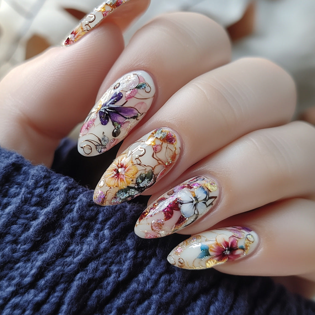 Nails with floral and butterfly design held against a textured blue fabric background