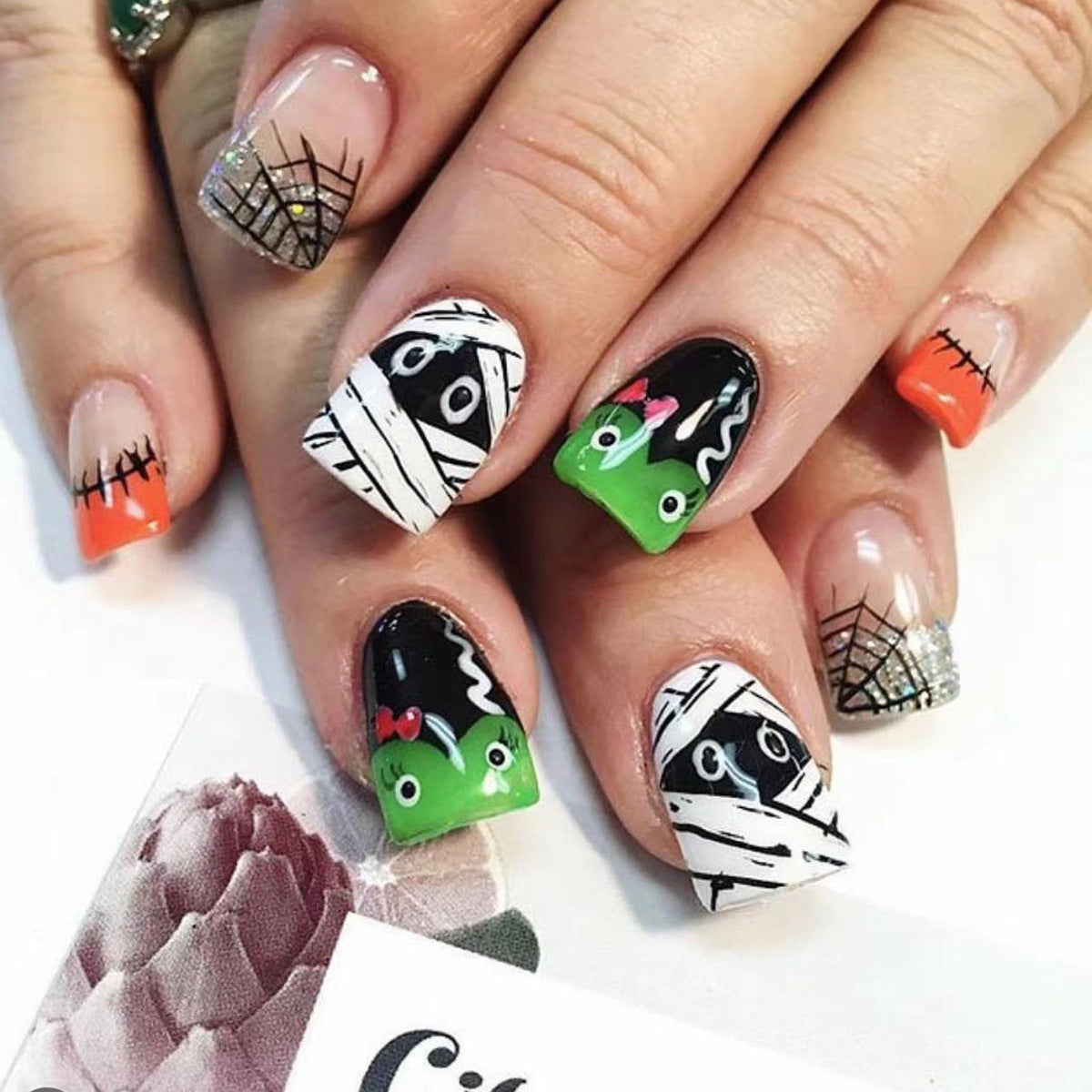 A set of press-on nails featuring a Halloween theme with black, white, green, and orange colors and character designs.