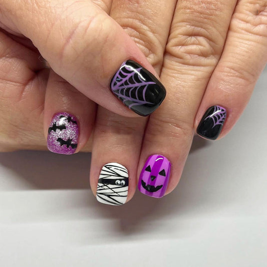 A set of press-on nails featuring a Halloween theme with designs including spiderwebs, a pumpkin, and a jack o lantern.