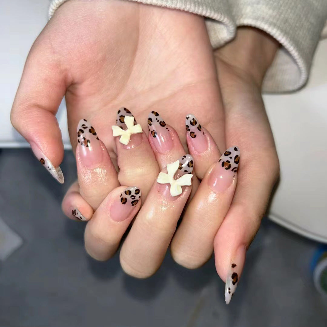 Hand with decorative nails featuring leopard print and white bow designs.