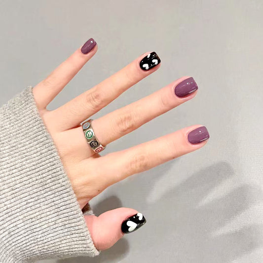 Hand with purple and black nail design on a gray background