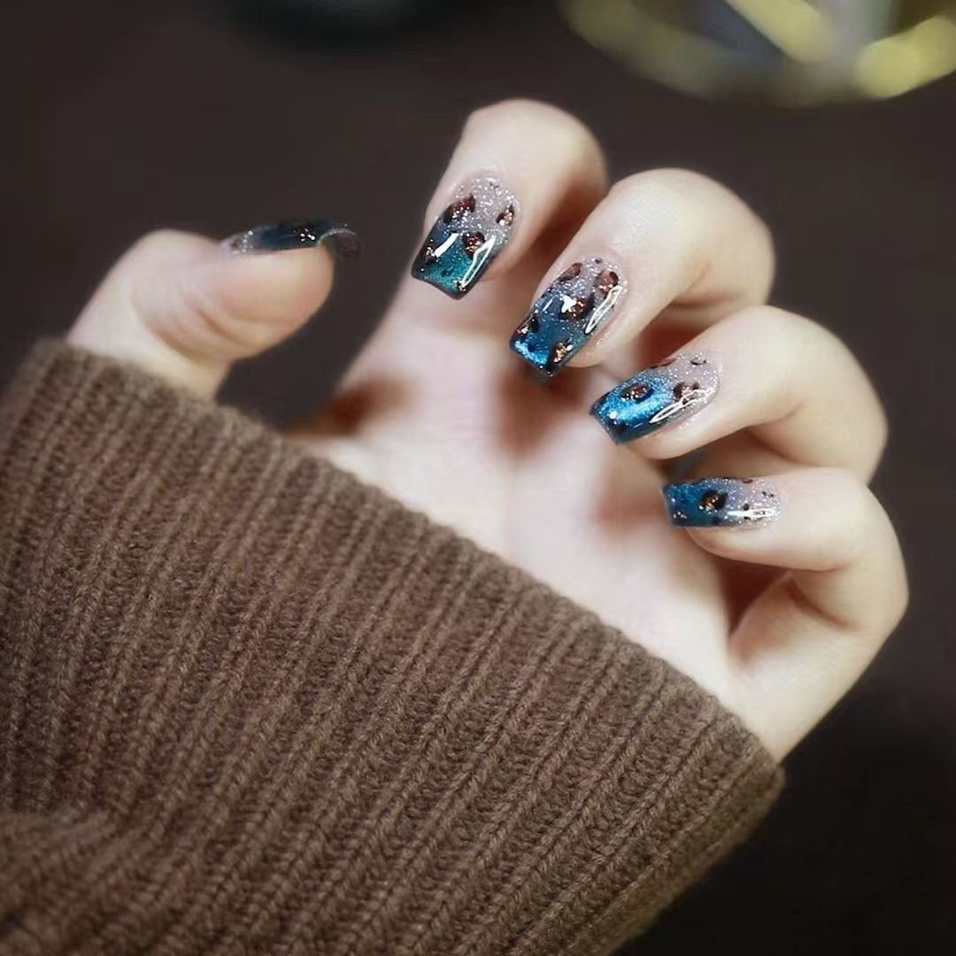 Hand with blue and silver nail art wearing a brown sleeve against a dark background