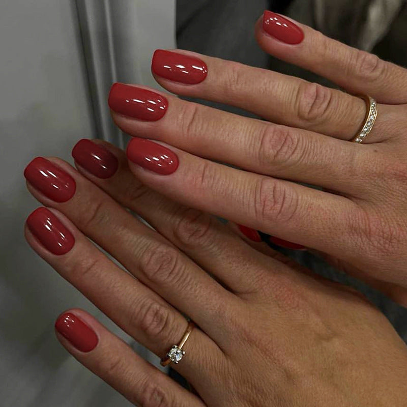 A set of press-on nails in a deep red glossy finish displayed on a person's hand.