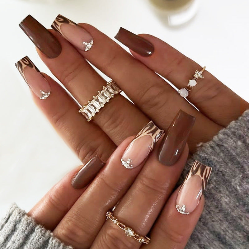 A set of press-on nails featuring long square shapes with a chic animal print tips and glittering accents on a beige background.
