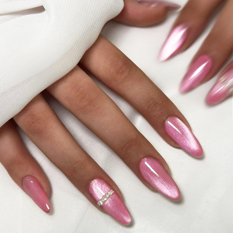 A close-up image of long almond-shaped pink nails with an iridescent shine and gemstone accents.