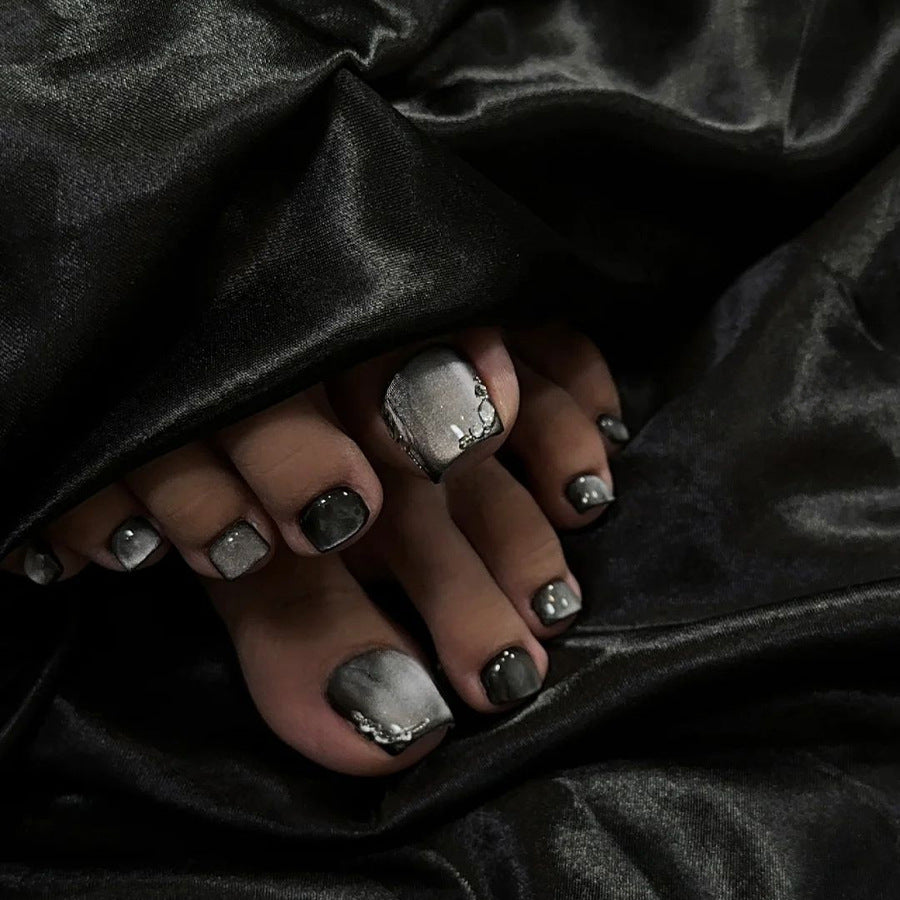 Close-up of toes with silver nail polish and rings on a dark fabric background