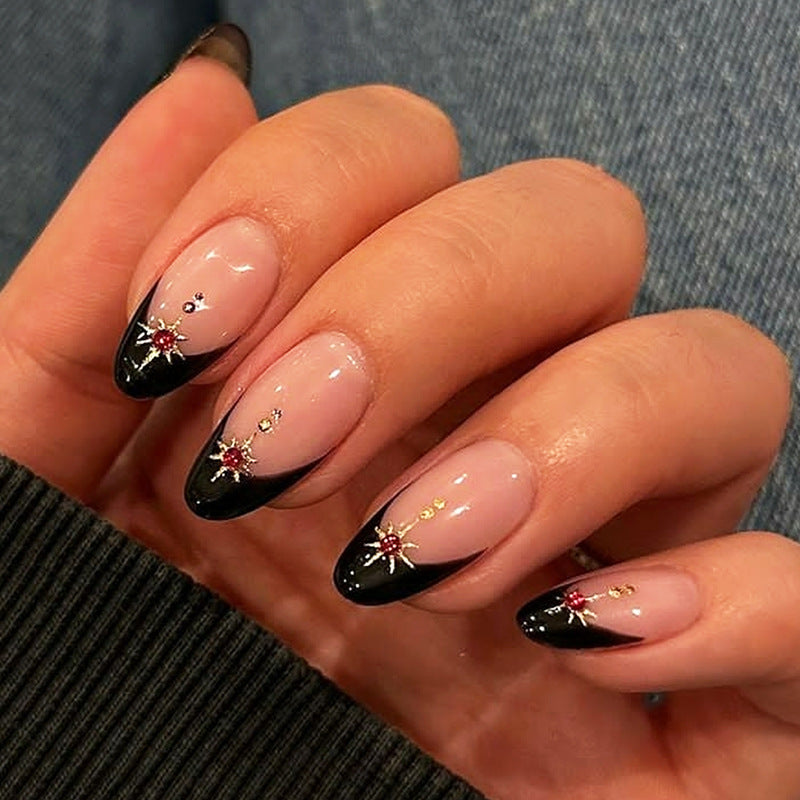 A set of press-on nails featuring an almond shape with a design of beige and black colors, and glittering star accents on the tips.