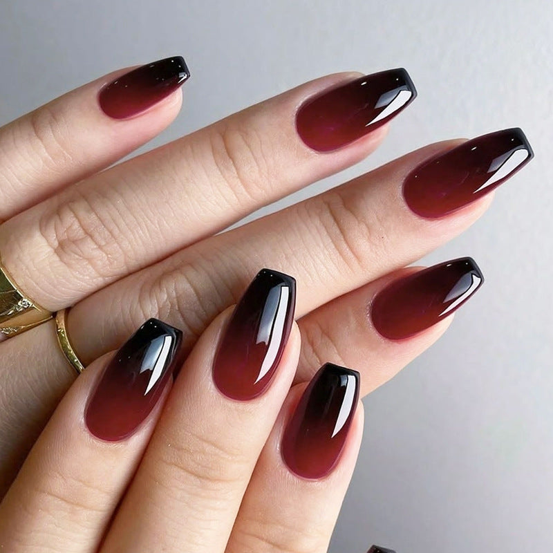 A set of press-on nails featuring a medium coffin shape with an ombre design transitioning from burgundy to black with a glossy finish.