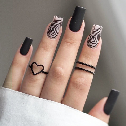 Close-up of a hand with black nail polish and heart-shaped rings on a neutral background