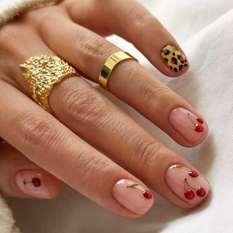 Hand with gold rings and cherry nail design on a white background
