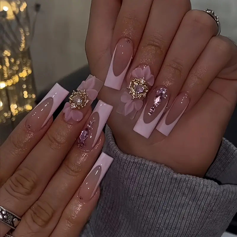 Close-up of hands with decorative nails featuring flowers and gemstones, with a blurred background.