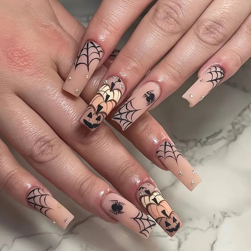 A set of long square press-on nails featuring orange and black colors with spider and pumpkin designs.