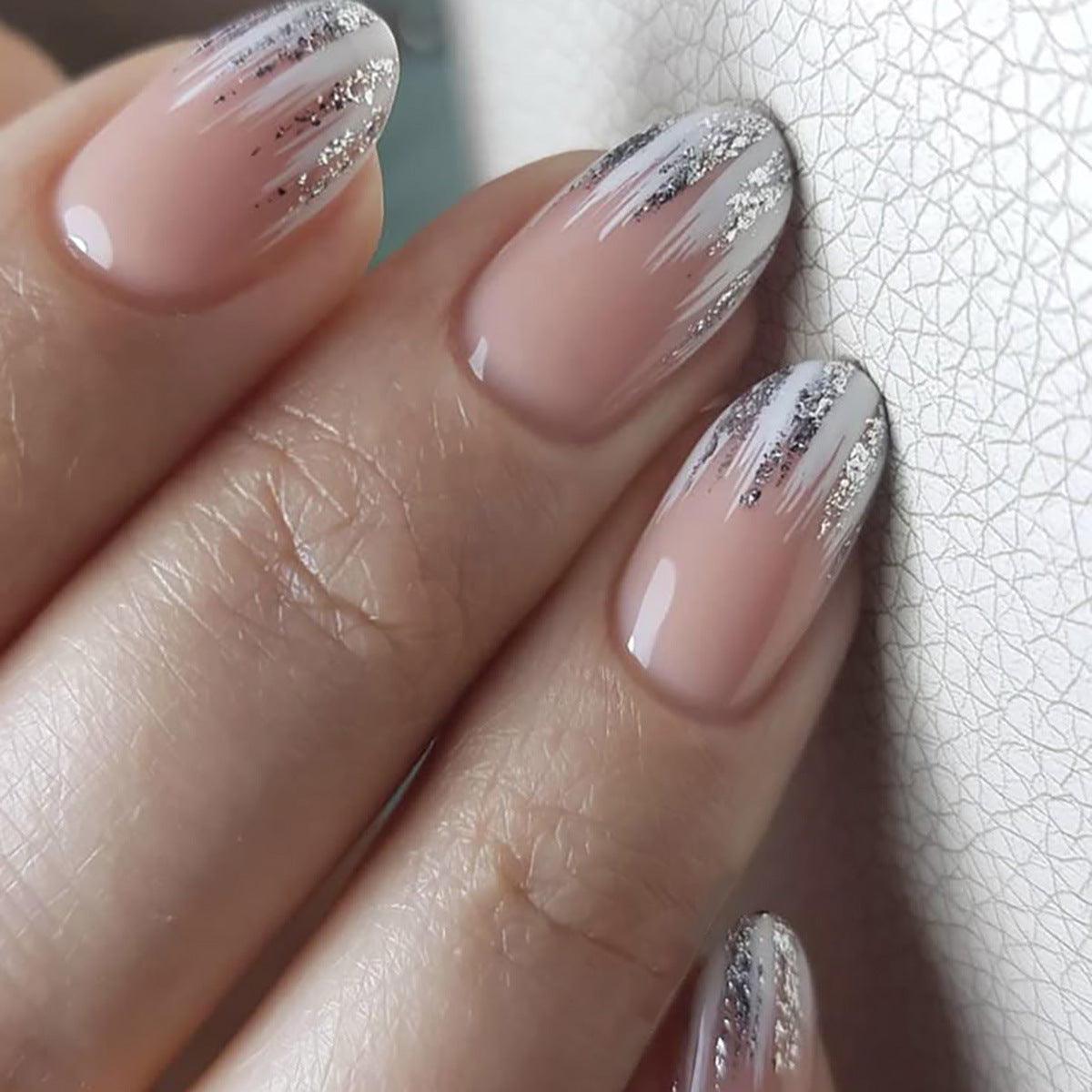 Close-up of a hand with pink nails and silver glitter on a textured white background