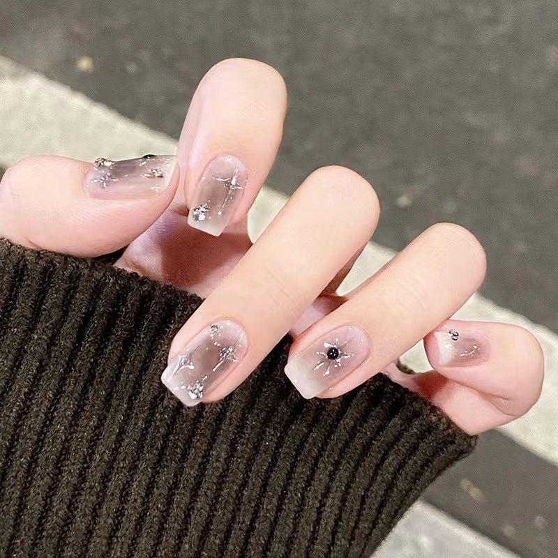 Close-up of a hand with clear nail polish and decorative elements, wearing a dark sleeve.