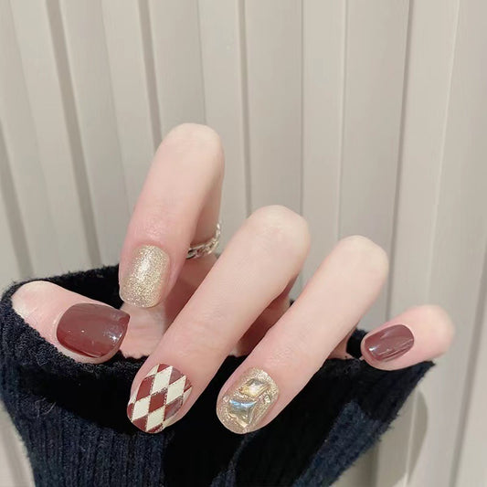 A set of press-on nails featuring a short square shape, adorned with a brown glittery finish and a unique harlequin design.