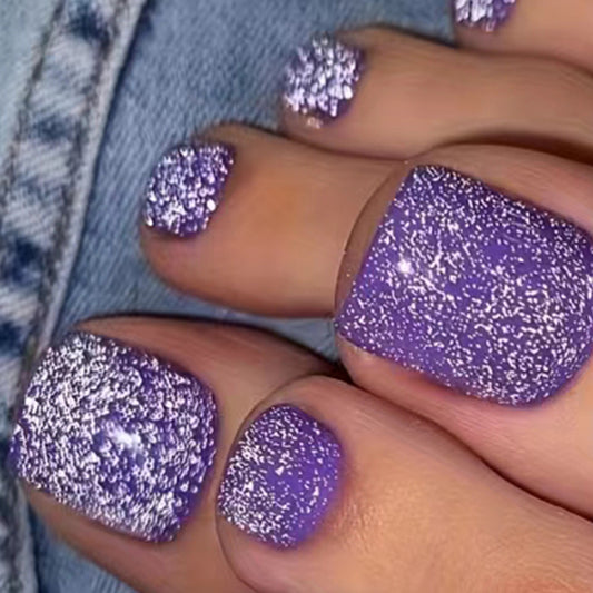 A close-up image of a person's feet wearing purple press-on nails with glitter overlaid on top.