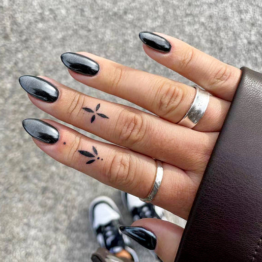 A photo showing a pair of hands with long, glossy black press-on nails featuring a gradient shimmer detail, and a silver ring on one of the fingers.