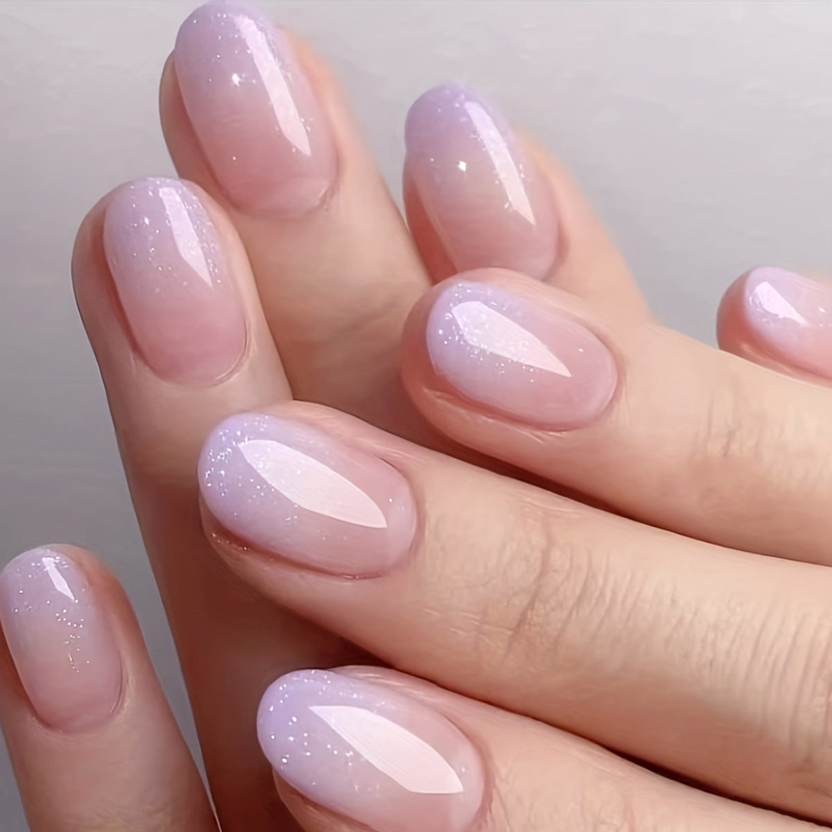 A set of press-on nails featuring a short oval shape with a lavender color and sparkle glitter finish.