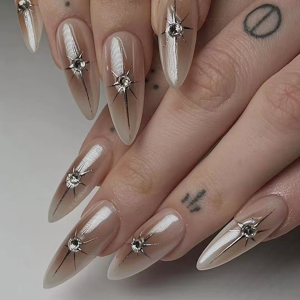 A set of beige press-on long nails with stiletto tips and crystal accents.