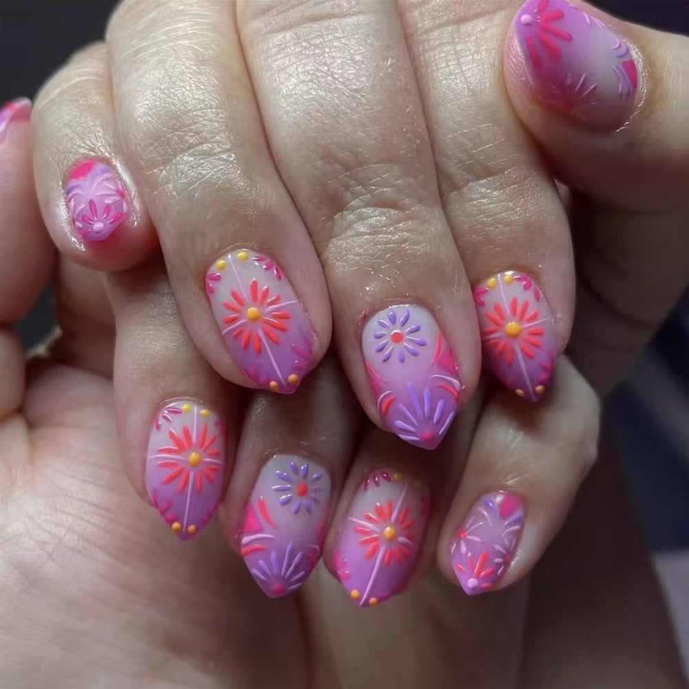 A set of press-on nails with an ombre design, featuring pink at the tips and transitioning to a lighter color towards the base, adorned with colorful floral patterns.