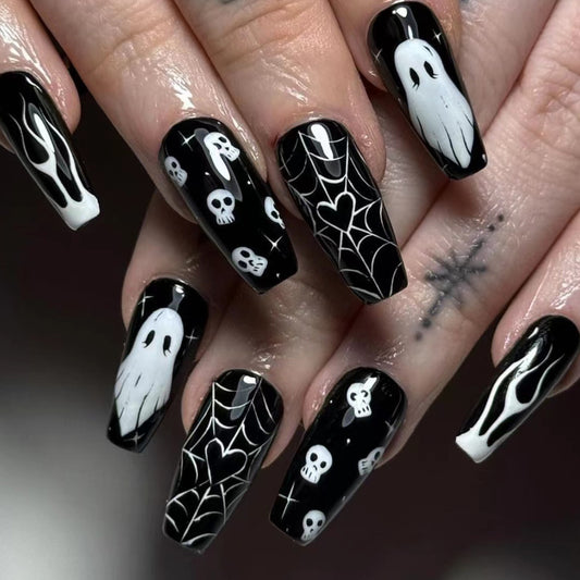 A set of long, black press-on nails with a unique spiderweb design featuring white skulls and ghosts.
