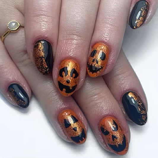 A set of press-on nails featuring a Halloween design with orange, black, and glitter, displayed on a hand.