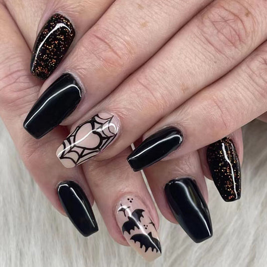 A set of long, black press-on nails with beige coffin-shaped designs and spiderweb patterns, displayed on a hand.
