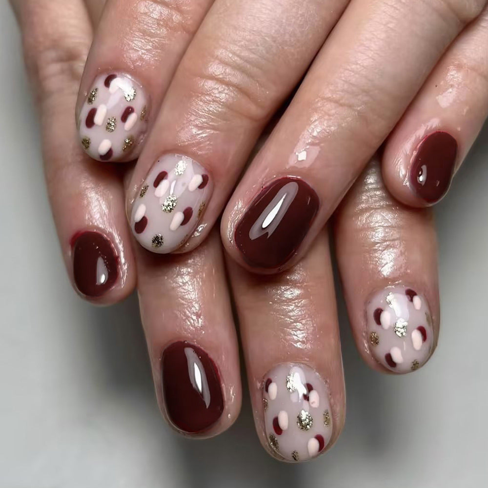 A set of press-on nails featuring a mix of burgundy, pink, and gold colors with gold accent dots.