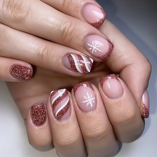 A set of press-on nails featuring a red glitter base with a snowflake and striped design, applied on a person's hand.