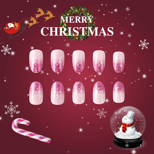 A set of press-on nails featuring a Christmas-themed design with pink ombre and glitter, displayed alongside holiday decorations.
