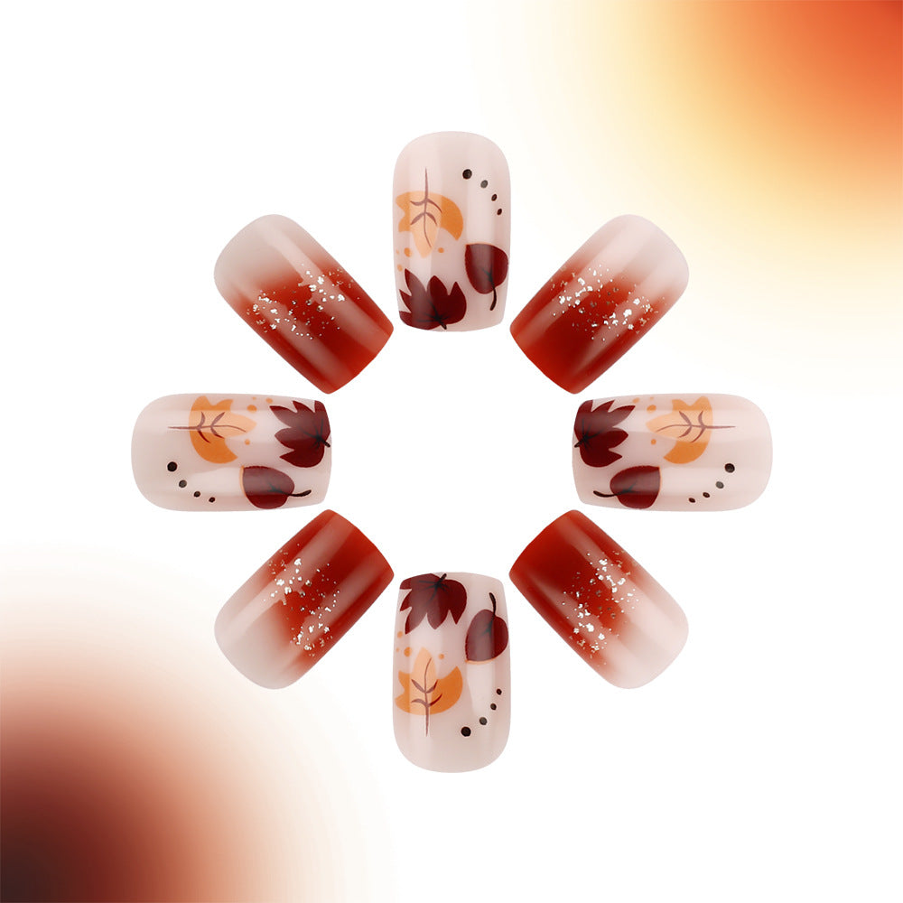 A set of press-on nails featuring a short square shape in a red ombre design with leaf patterns.