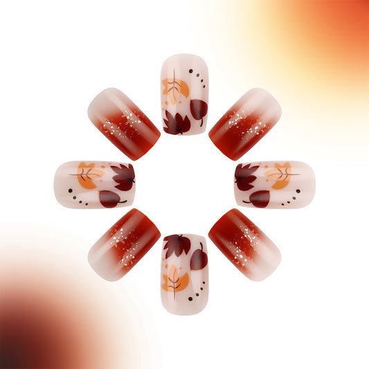 A set of press-on nails featuring a short square shape in a red ombre design with leaf patterns.