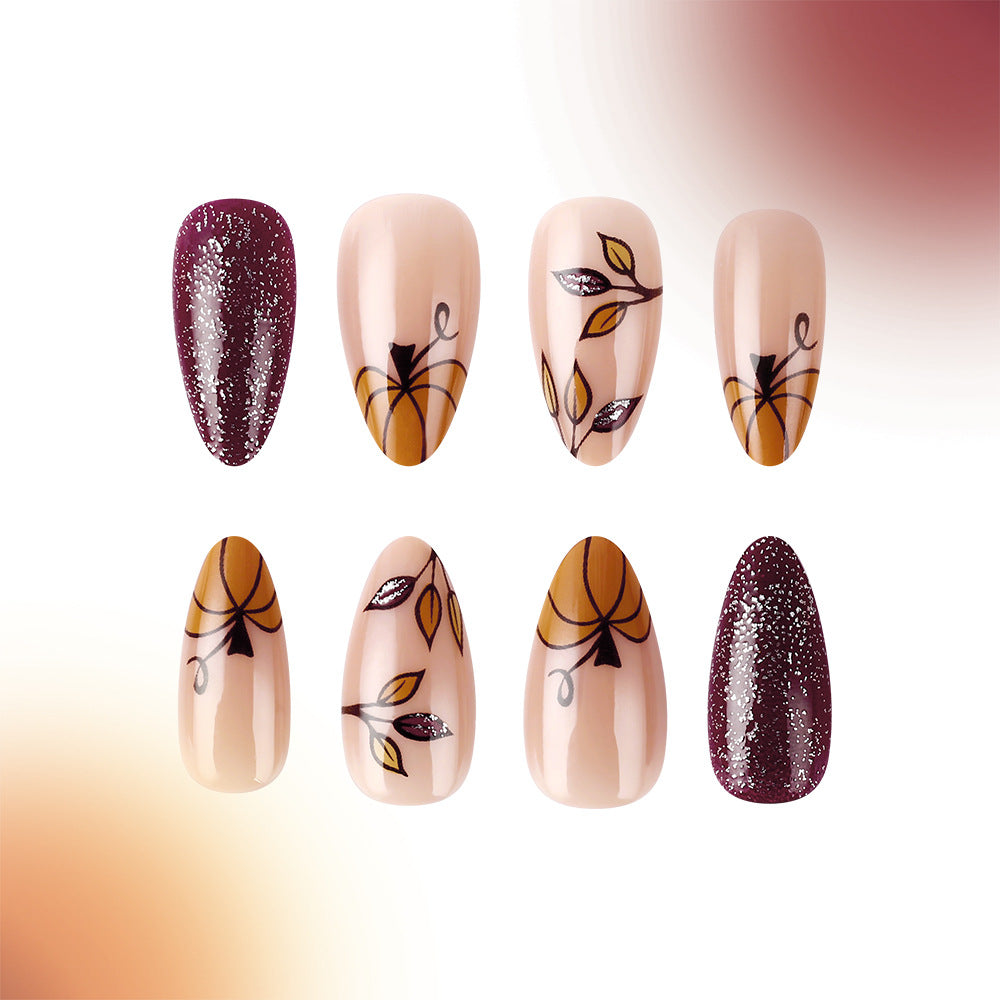 A set of long almond-shaped press-on nails with intricate leaf designs and glitter accents, transitioning in color from beige to burgundy.