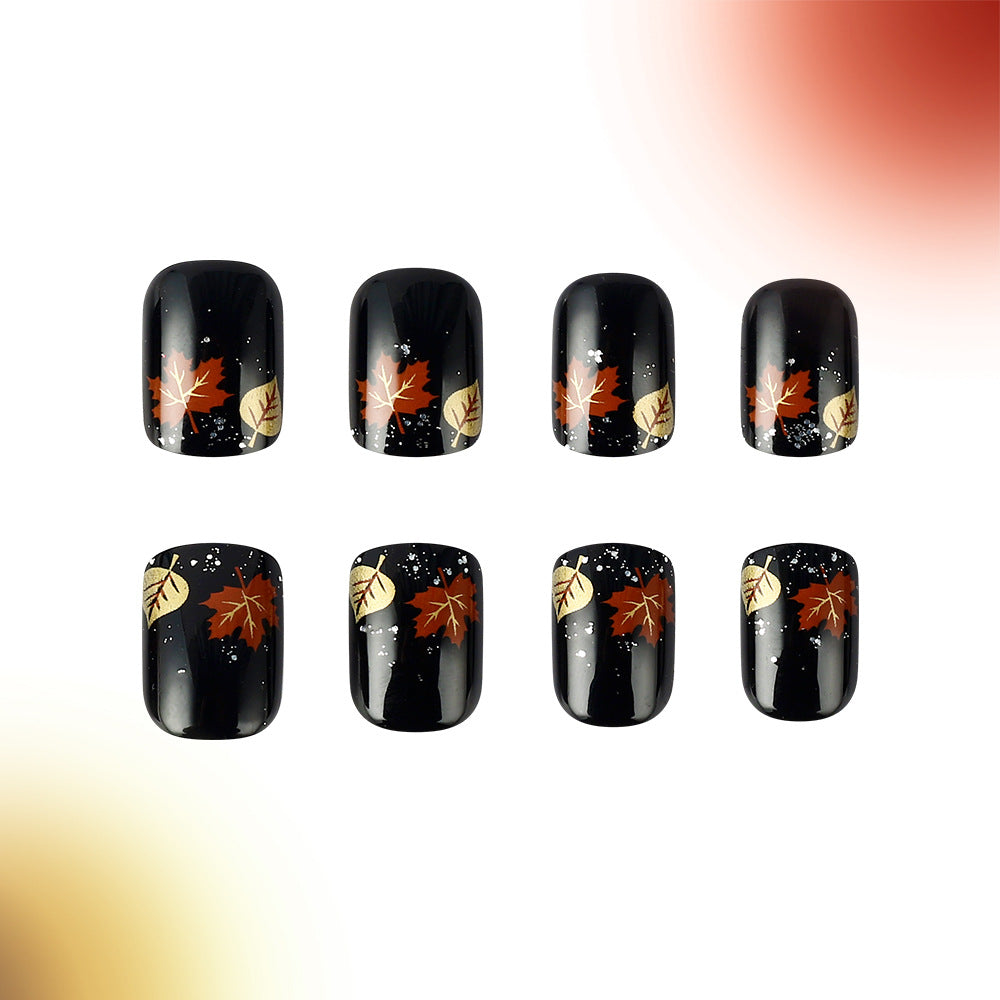 A set of eight press-on nails featuring a fall leaf design with sparkling accents on a black background.