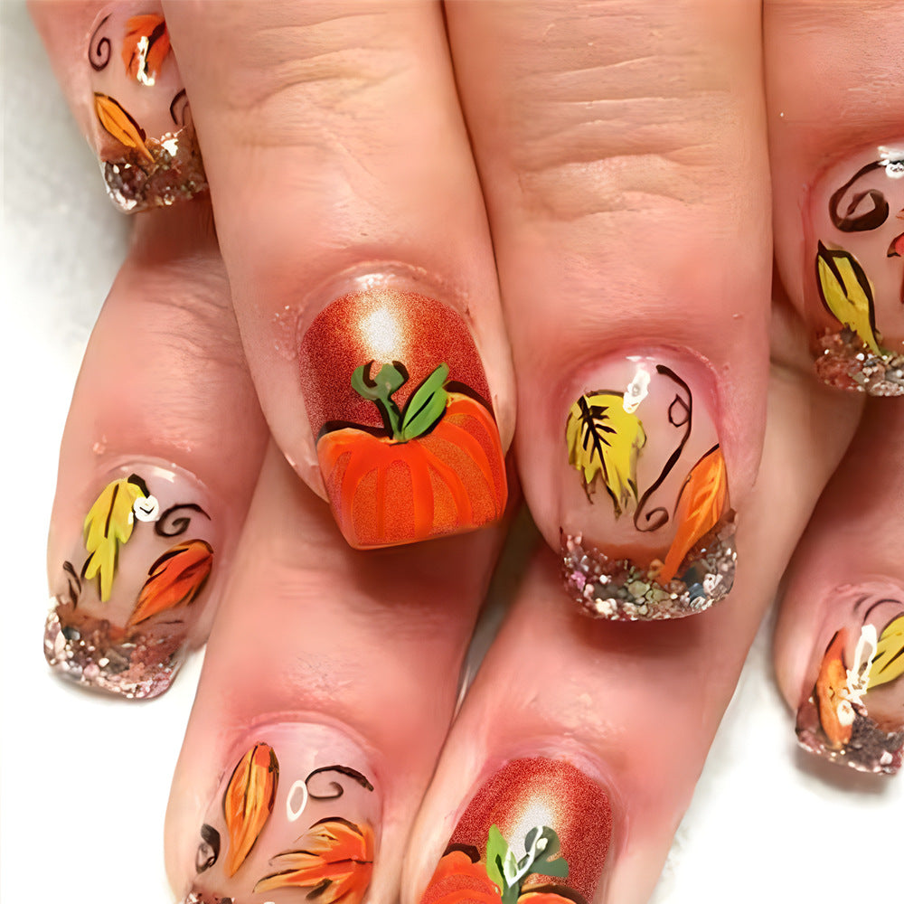 A set of press-on nails featuring a variety of autumn-themed designs including pumpkins, leaves, and glitter.