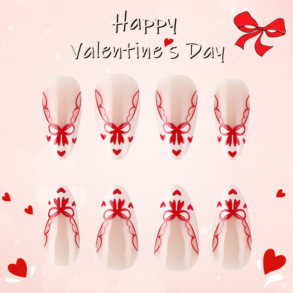 A set of artificial nails in medium almond shape with a soft pink base and red bow designs, displayed against a Valentine's Day themed background.