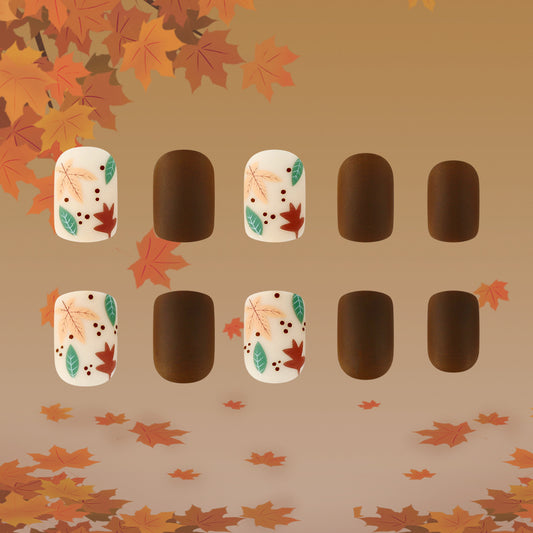 A set of short square nails with a brown base and cream design featuring leaf patterns, presented against a backdrop of autumn leaves.