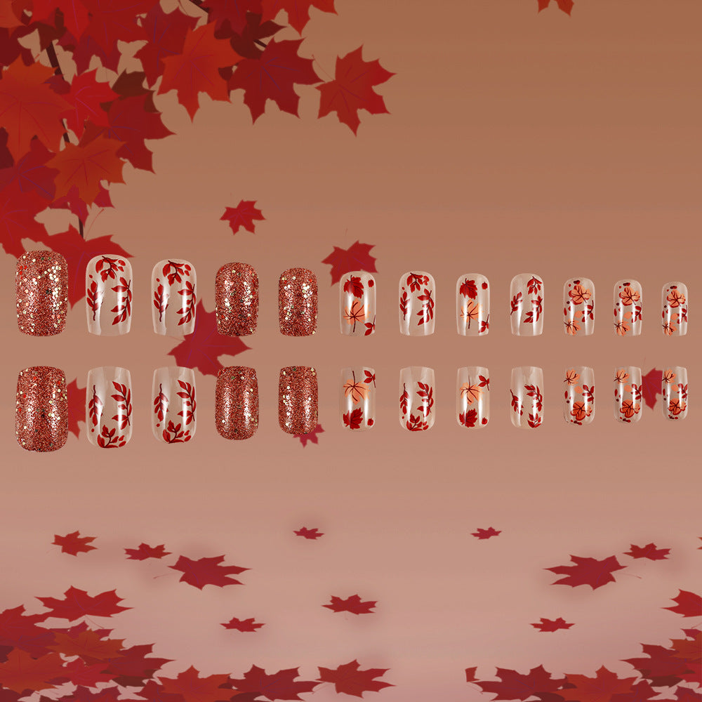 A set of red and transparent nail extensions with glitter and leaf patterns, displayed in a line against a background of red leaves.
