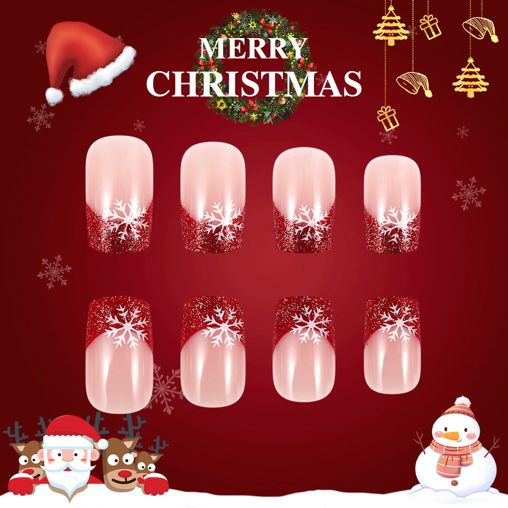 A set of red glitter ombre press-on nails with a snowflake design, displayed in a festive winter setting with Christmas decorations.