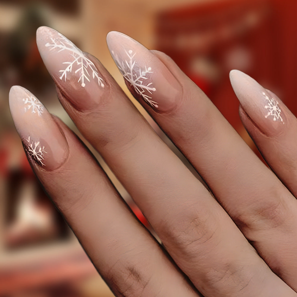 Close-up of a hand with almond-shaped nails featuring white floral designs on a blurred background.