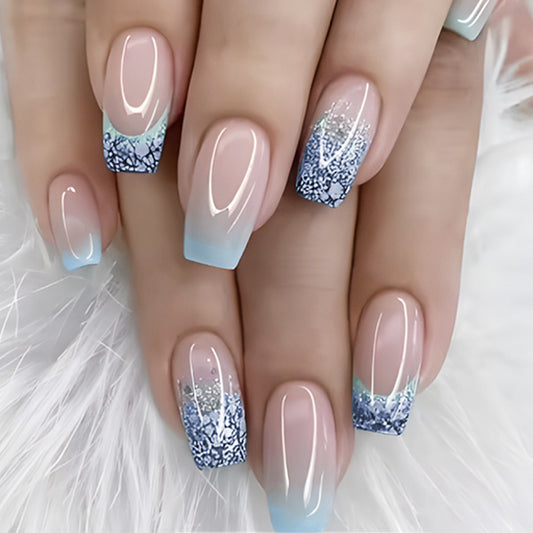 A set of press-on nails featuring a medium coffin shape with a blue ombre design and an intricate floral pattern near the tips.