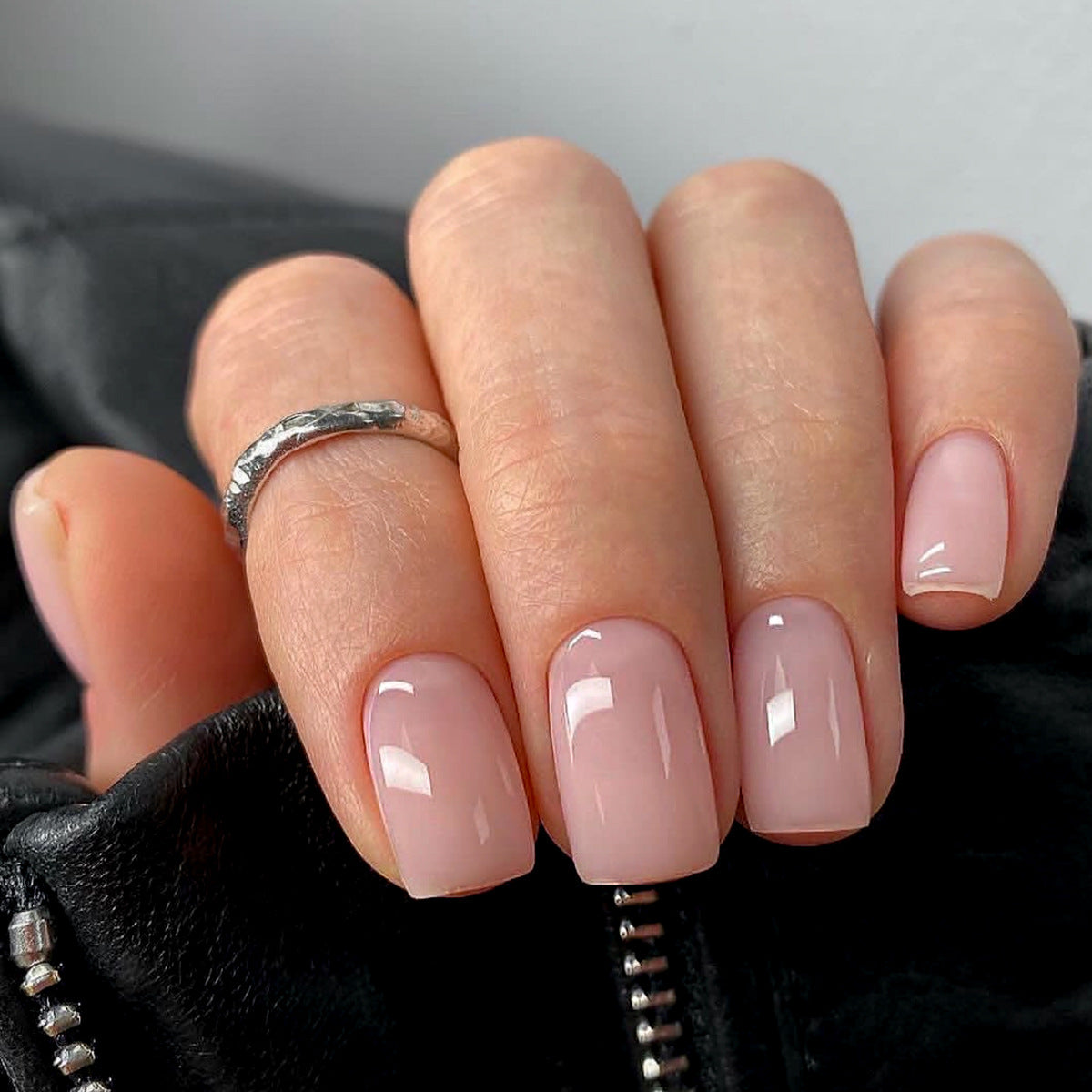A hand with medium pink glossy finish press-on nails, shown resting on a black leather surface.