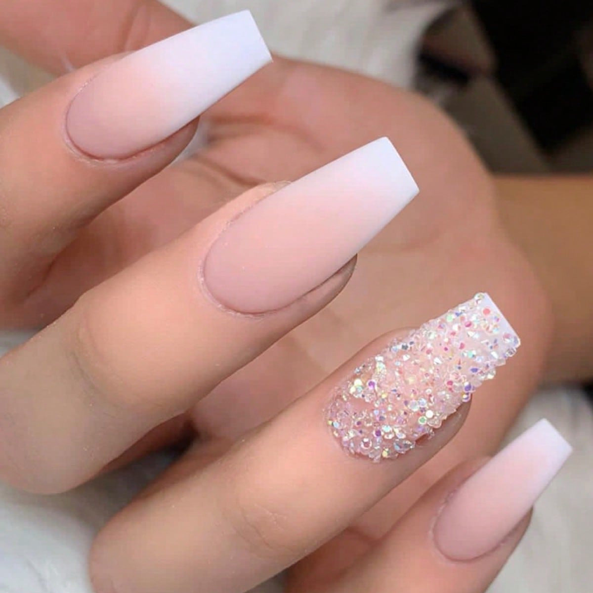 A set of long, white and pink ombre press-on nails with glitter accents, displayed on a hand.