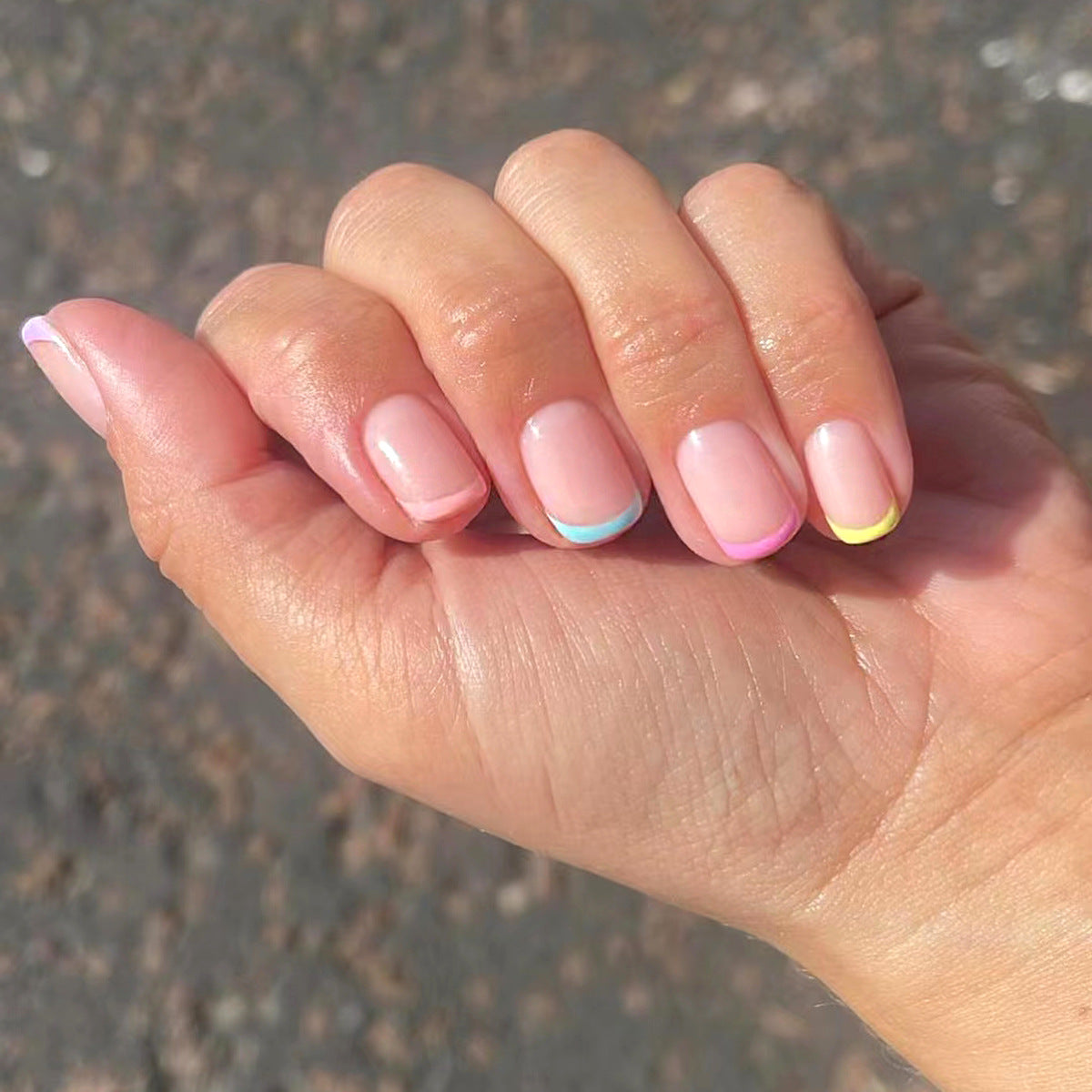 Close-up of a hand with pastel nail polish on a textured surface